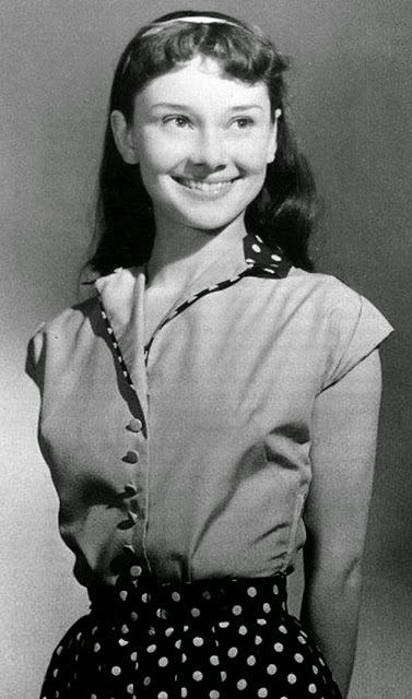 Jeune femme souriante avec des cheveux bruns, portant un haut à boutons et une jupe à pois.